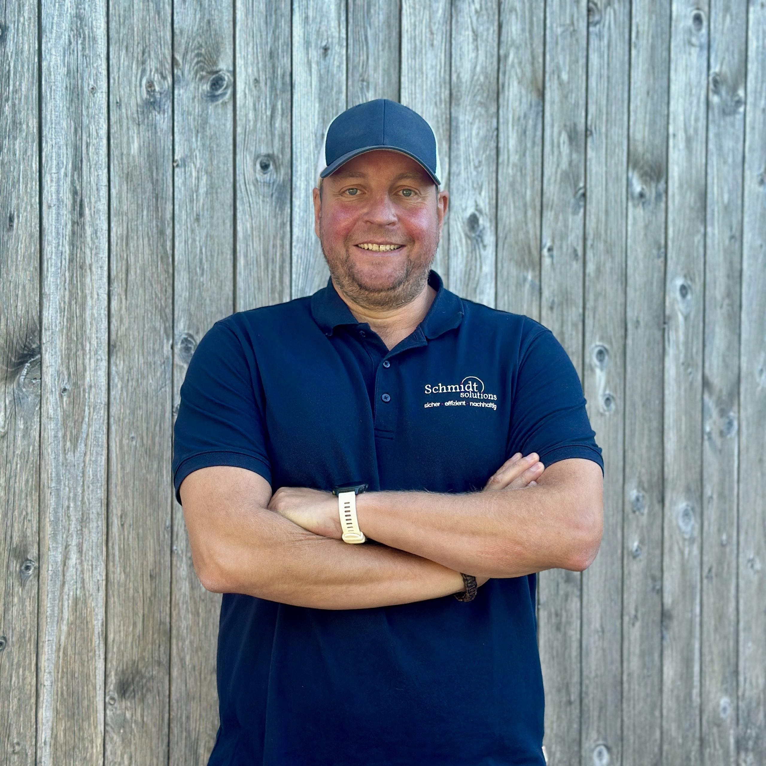 Mann mit blauem Poloshirt vor einer Holzwand
