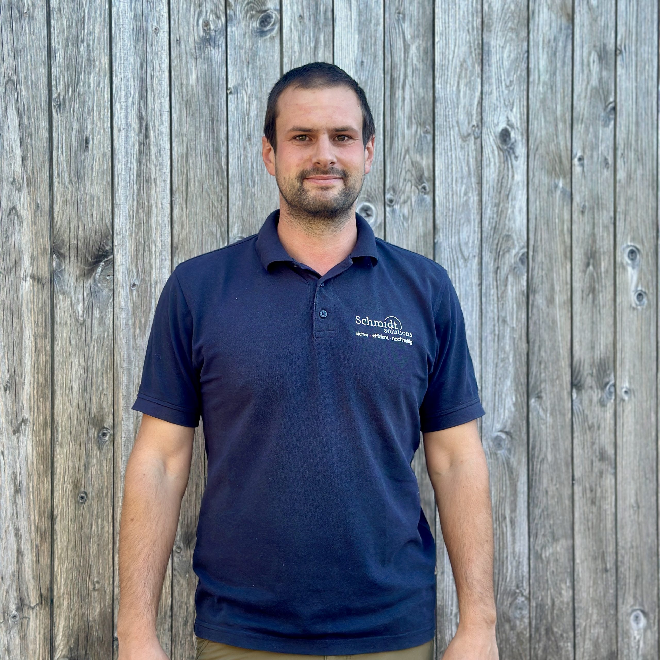Mann in blauem Polohemd vor einer Holzwand